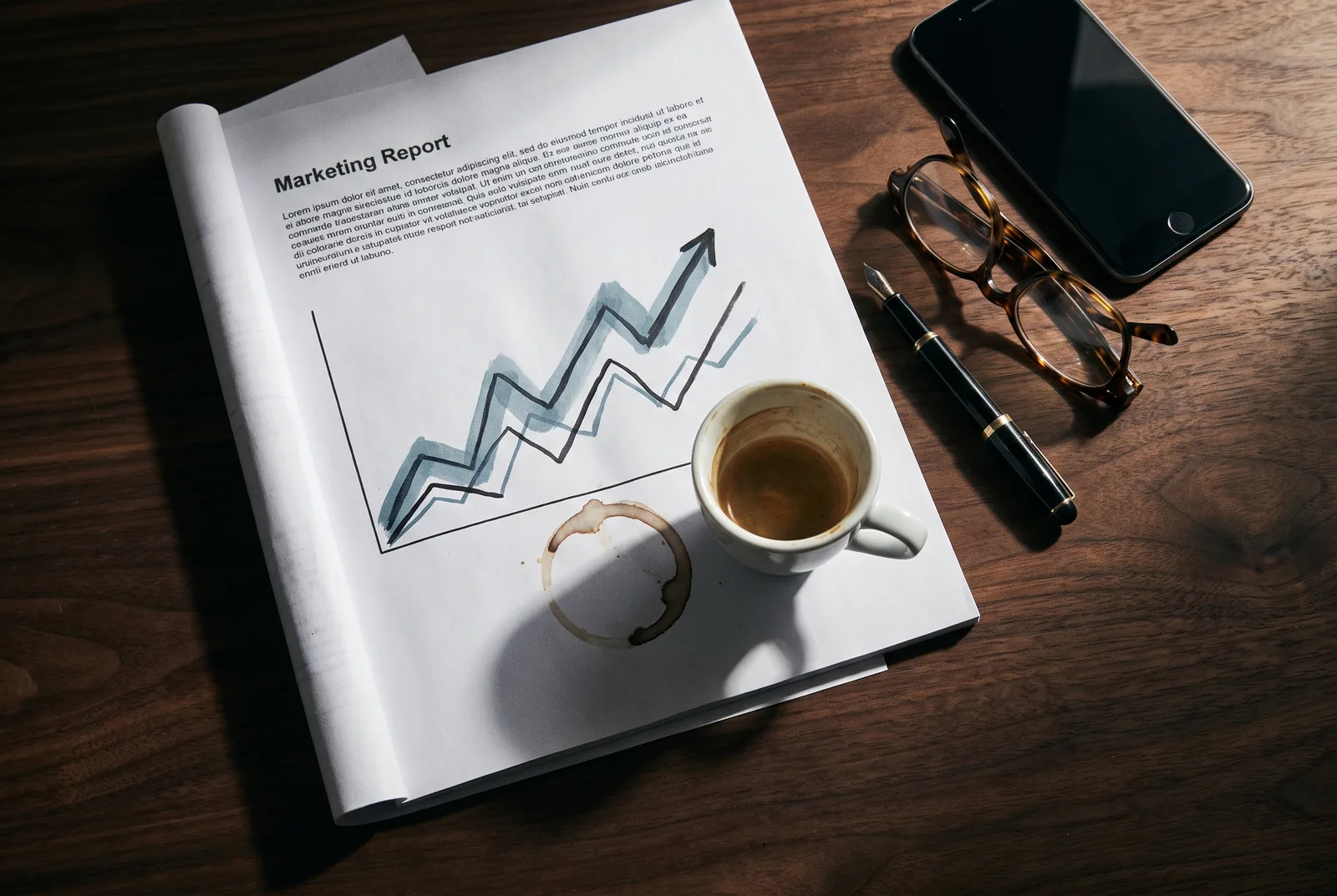 A printed marketing report with a chart, a cold coffee and reading glasses on a desk